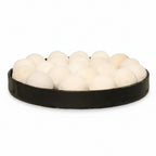 A black oval tray filled with numerous small white pom-pom balls, photographed against a plain white background.